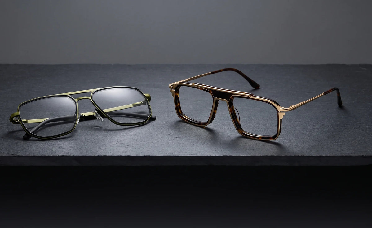 Glint in green metal beside Cord in tortoise and gold, two eyeglasses with double bridges on dark graphite slate.