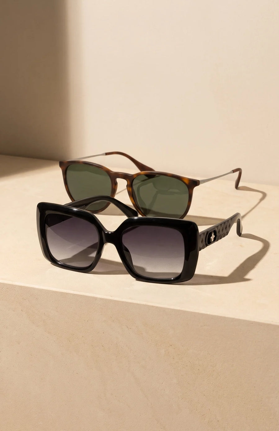 Black square and tortoise round sunglasses on a sunlit stone ledge.