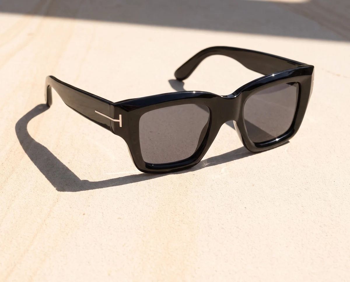 Girder thick black square sunglasses with smoke grey lenses on sunlit sandstone.