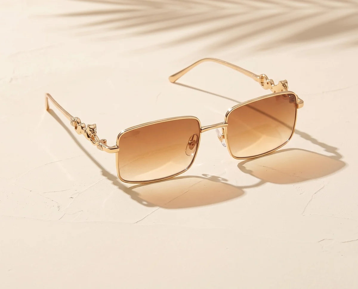 Kestrel gold rectangle sunglasses with brown gradient lenses on pale sunlit plaster.
