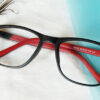 Black and Red Frame Eyeglasses placed on blue and white fabric with peacock feather